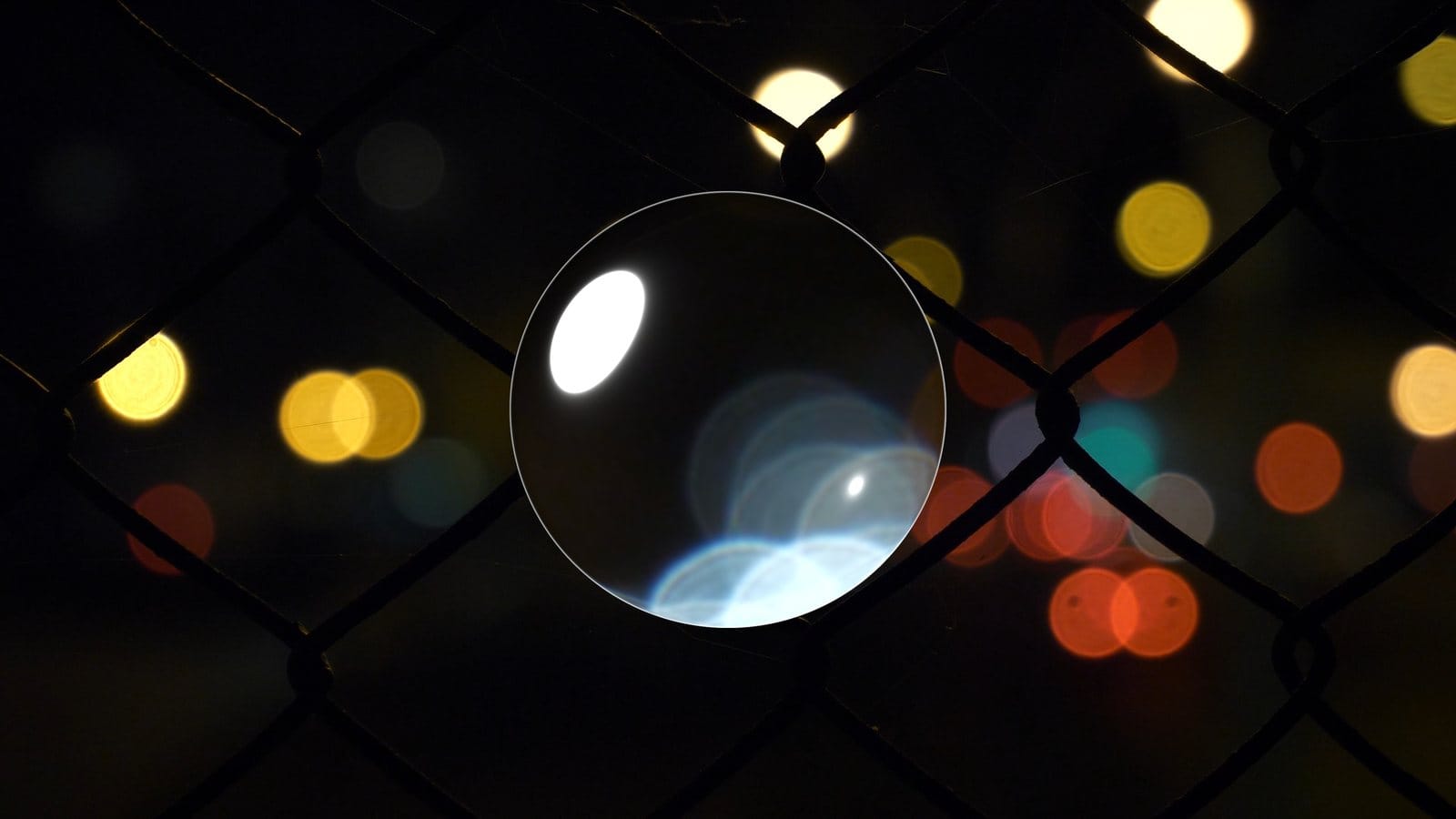 Clear sphere on a chain-link fence with city bokeh
